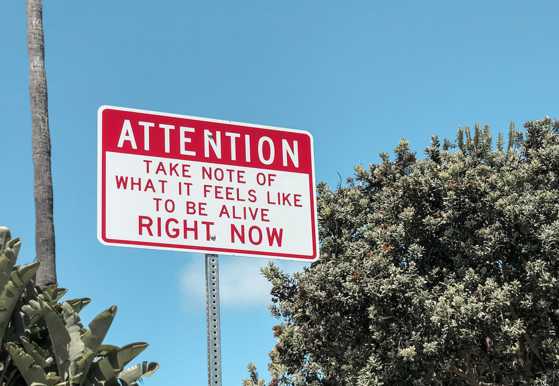 Motivational street sign against a bright blue sky in Laguna Beach, California.
