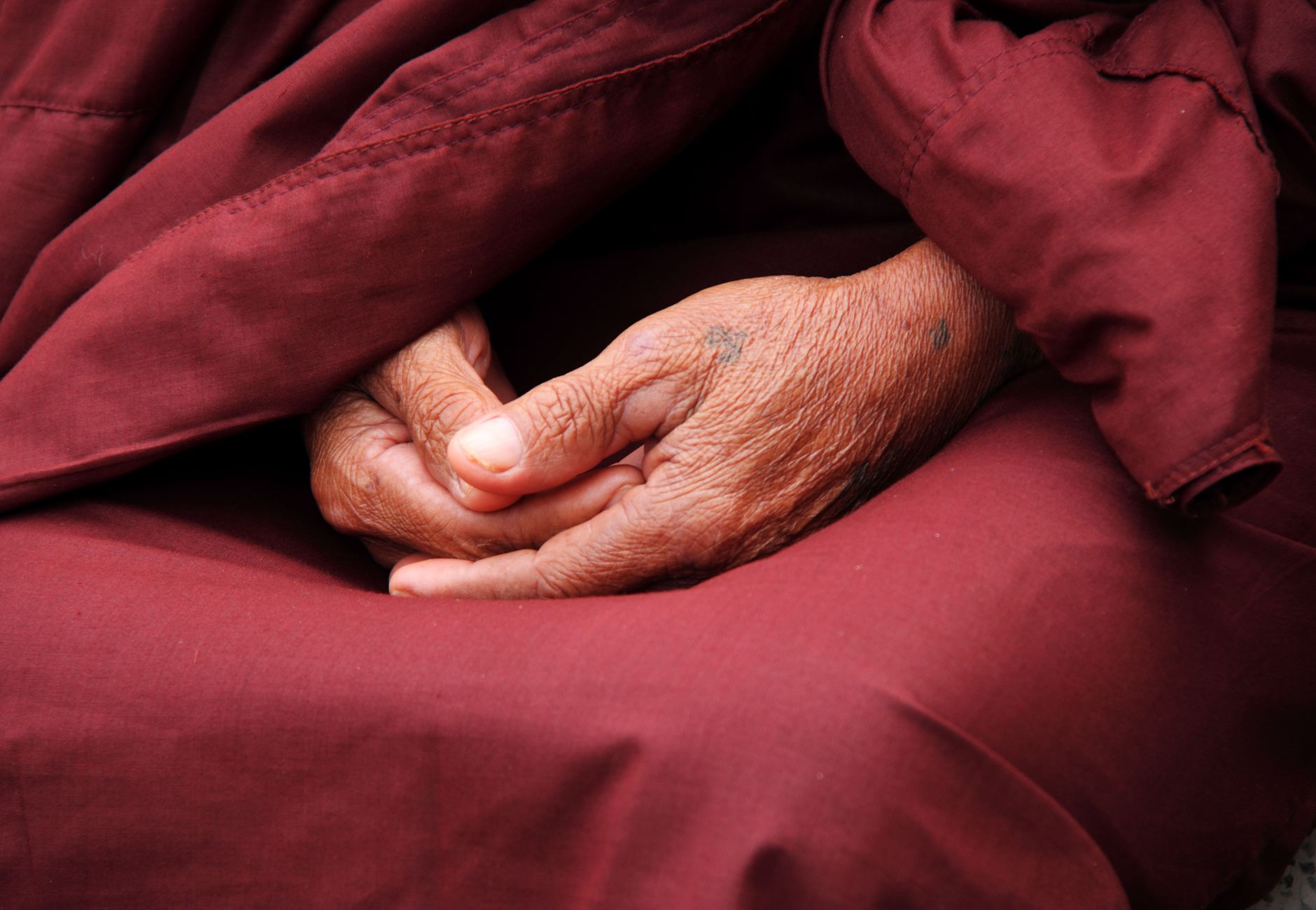 Close-up of a monk's hands in prayer, wrapped in maroon robe, symbolizing peace and spirituality.