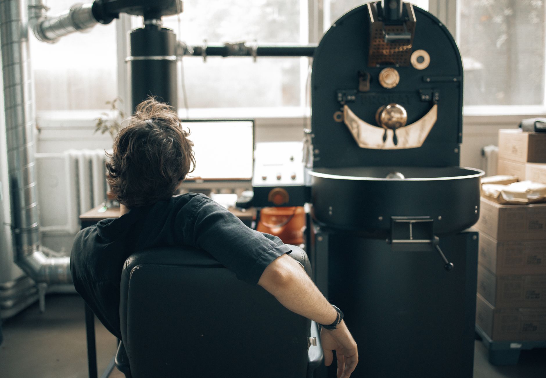 Man observes coffee roasting process in industrial setting with modern equipment.