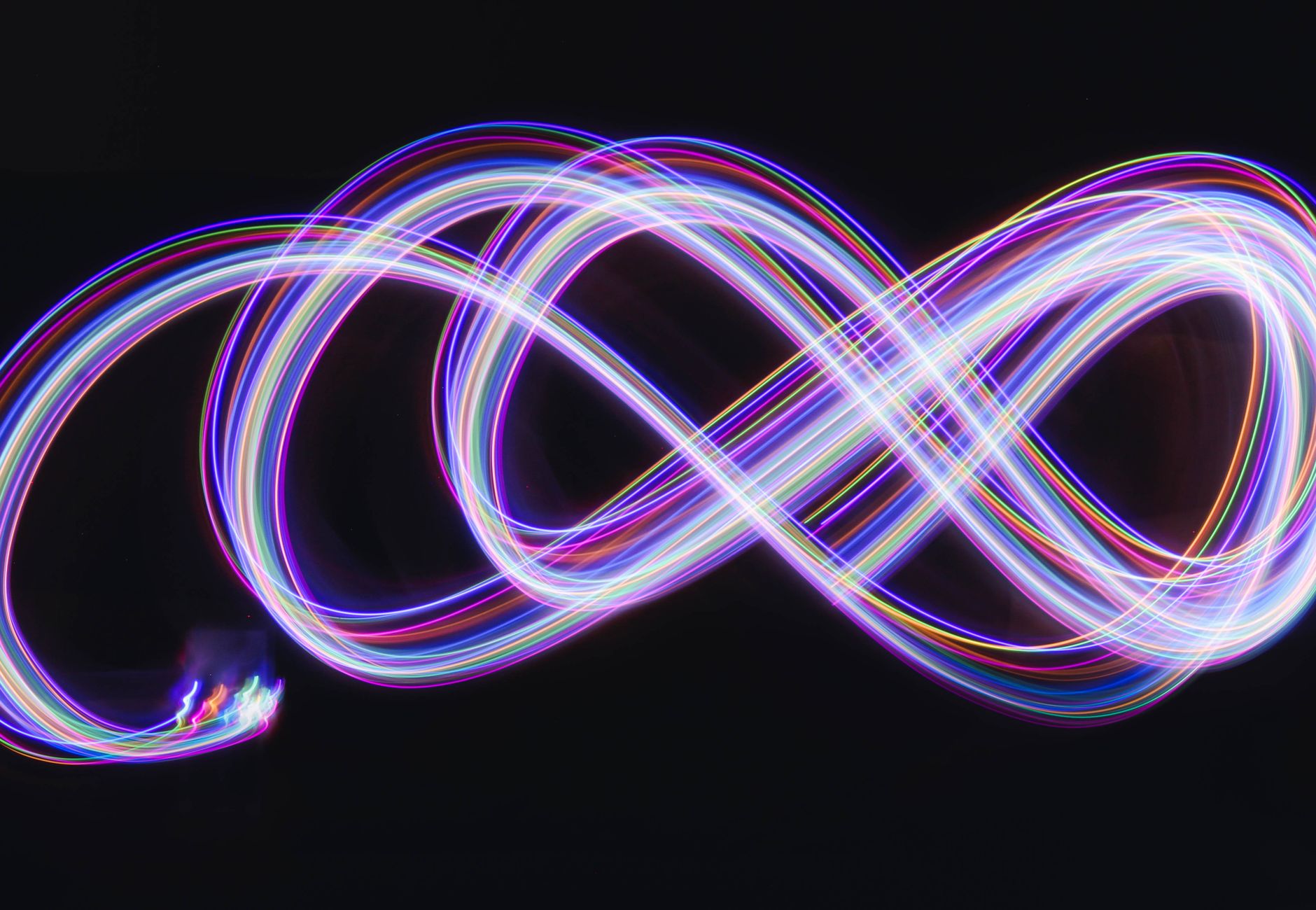 Abstract long exposure photography of colorful neon light streaks forming an infinity symbol.
