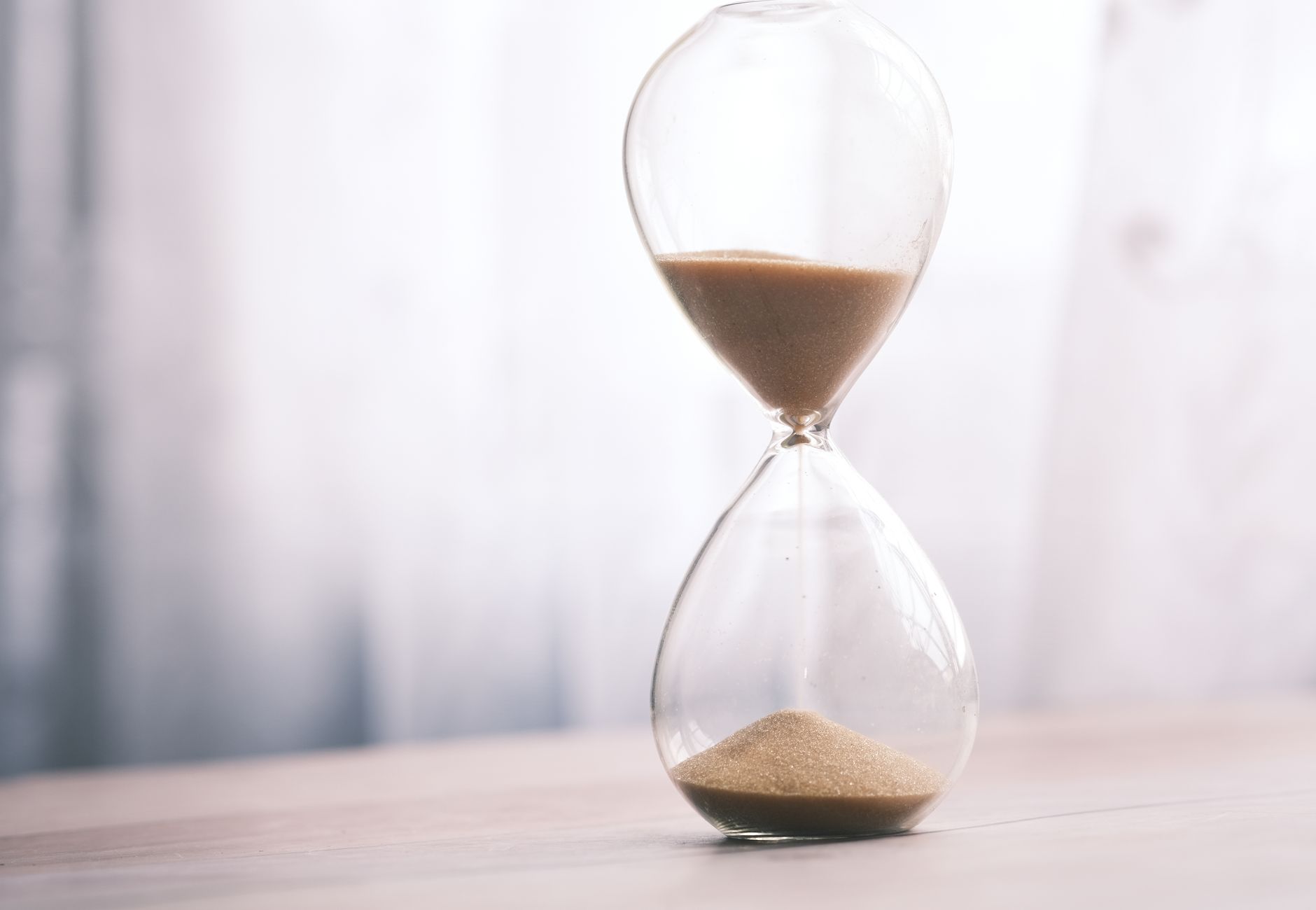 Minimalist hourglass filled with sand symbolizing time and patience, against a soft background.