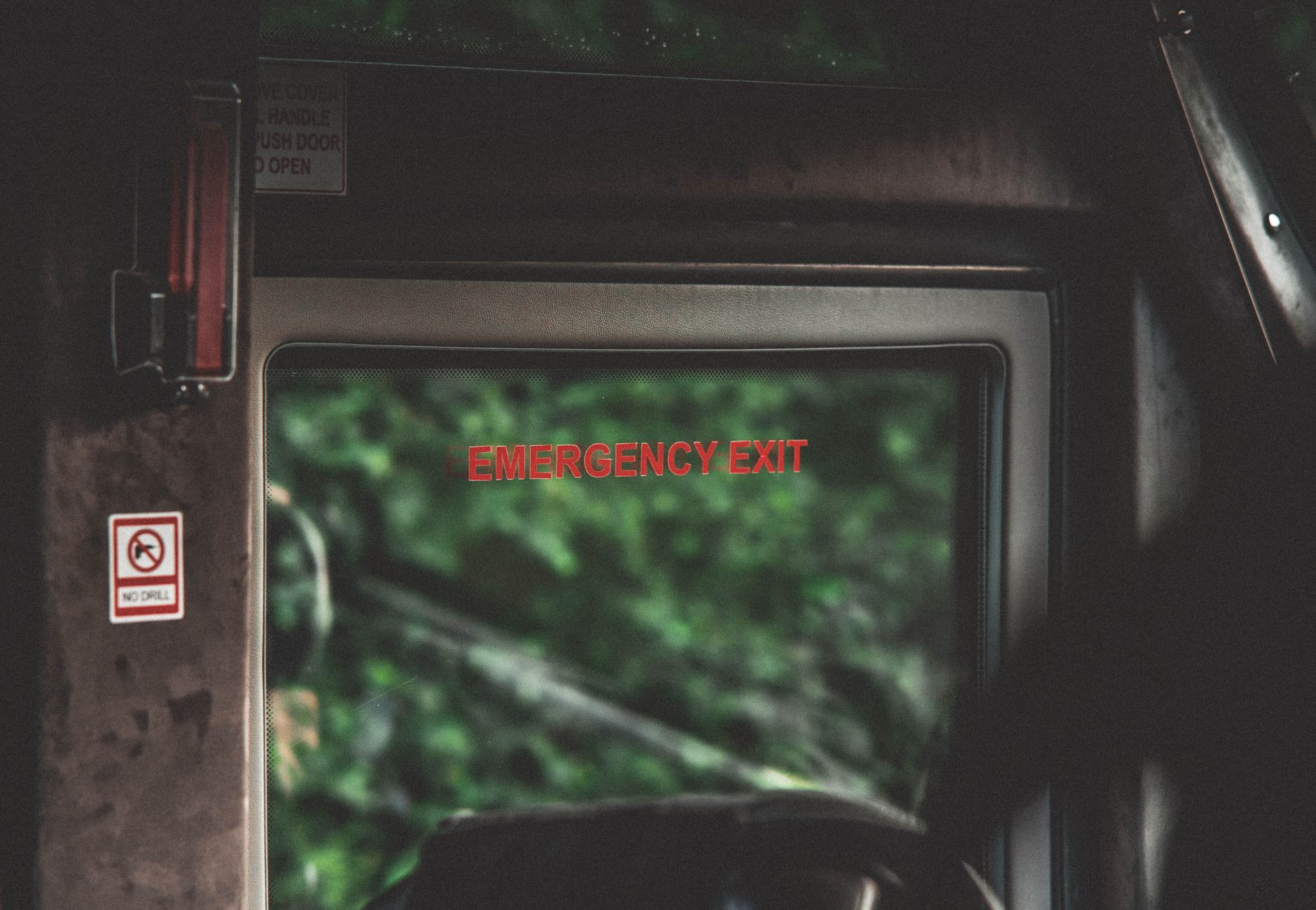 Interior of a vehicle showing an emergency exit sign with a green outdoor view.